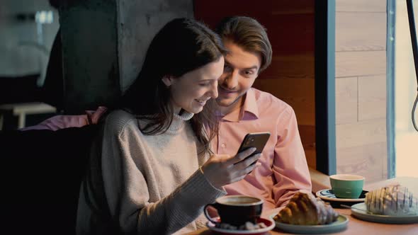 Couple in the Cafe Holding Smartphone Celebrate Online Betting Victory