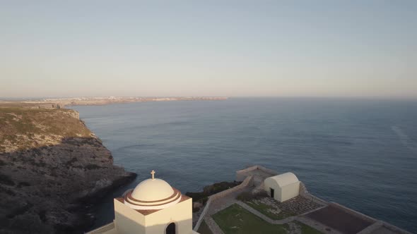 Drone flying out from cliffside chapel from fort of Santo António de Belixe alt