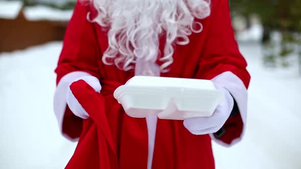Food delivery service containers in hands of Santa Claus outdoor in snow. Christmas eve promotion. R alt