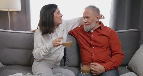 Smiling Grown Up Daughter Communicating with Old 80s Father Sitting Together on Comfortable Couch at