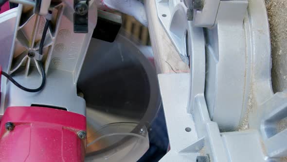 Vertical Shot Male Carpenter in Gloves Cuts Off Wooden Workpiece on Mitre Saw Closeup