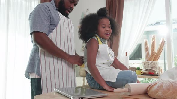 African American dad wearing aprons on little girl in kitchen at home. Happy family, domestic life
