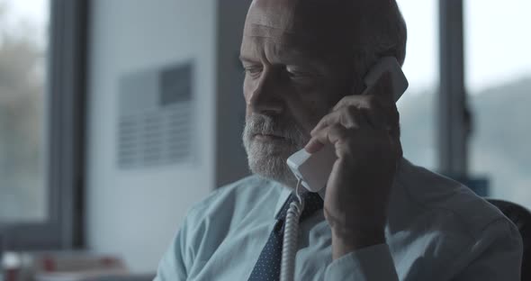 Corporate businessman sitting at desk in the office and answering phone calls