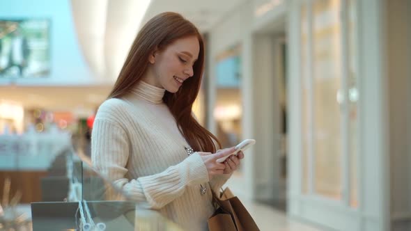 Tracking Shot of Smiling Redhead Female Using Smartphone Standing in ...