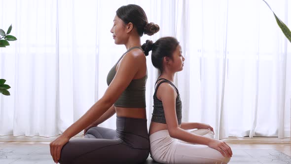 Fit young woman in sportswear training a little girl to yoga pose and exercise at home.