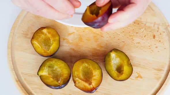 A man arranges sliced plum halves on a yellow wooden board. Large juicy dark blue plums on a white