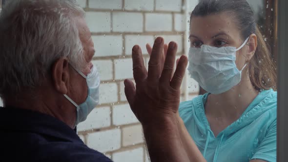 Old Man And Woman Touch Palms Of Their Hands Through Glass Window In Quarantine alt