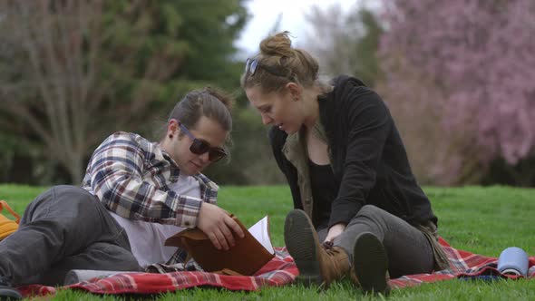 Two young people at park on blanket looking at book together