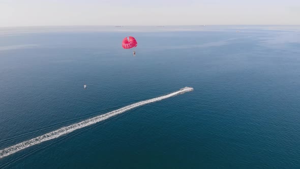 Towing Red Parachute Behind a Jetski Over the Sea Along the Beach at Sunset. alt