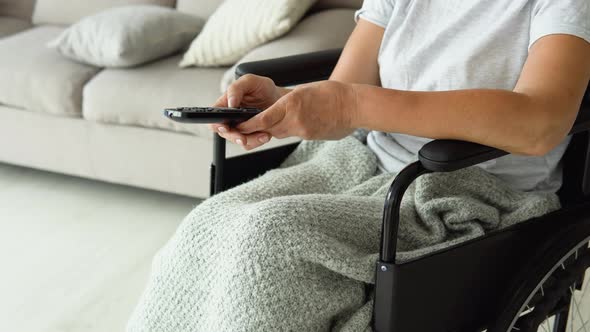 Senior Lady in Wheelchair Watching Tv in Living Room Holding Remote Control Changing Tv Channels alt