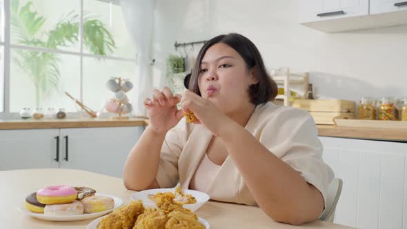 Asian plus size fat girl feeling hungry and happy to bite fried chicken and sweet donut on table. alt