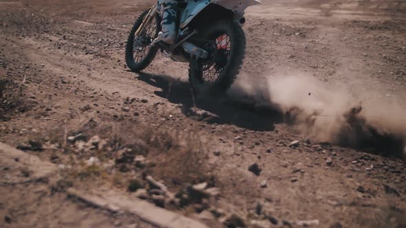 A biker rushes along a sandy track, leaving behind a cloud of dust, close-up. Slow motion.