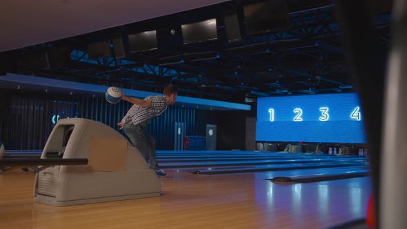 In a Plaid Shirt a Man in a Bowling Alley Throws a Ball in Slow Motion and Knocks Down Skittles alt