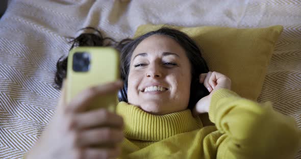 Authentic shot of woman on the bed listening to music and singing