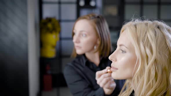 Master of Makeup Is Applying Powder on Face Skin of Beautiful Blonde Client Woman in Beauty Shop alt
