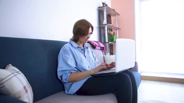 Woman printing on laptop sitting on couch. Remote work concept.