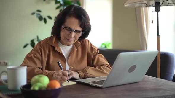 Woman Writing and Using Computer During Self Education at Table in Apartment Room alt