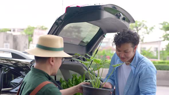 4K Asian man plant shop owner helping customer put potted plants in car trunk. alt