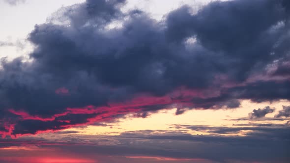 A large dark cloud with a glimmer of light from the red setting sun, timelapse
