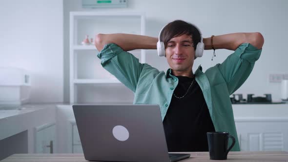 Young Man in Wireless Headphones is Resting After Working at a Computer Enjoying Good Mood alt