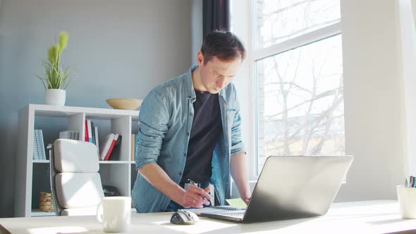 Young male entrepreneur works at home office at the computer. alt