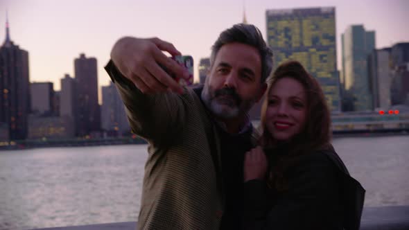 Couple in New York City taking cell phone selfie with city skyline in background