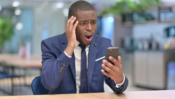 African Businessman Reacting To Failure on Smartphone in Office  alt