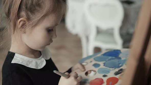 Child is painting with paintbrush on canvas
