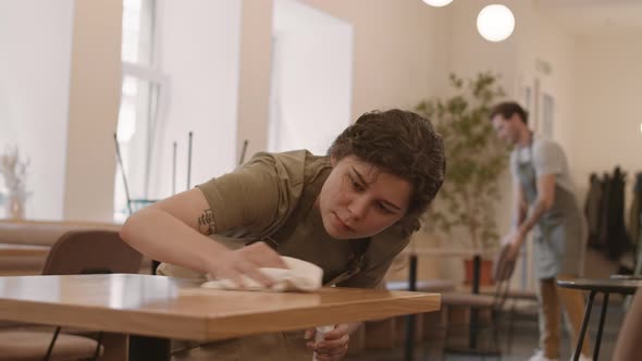 Female Cafe Worker Wiping Table Scrupulously alt
