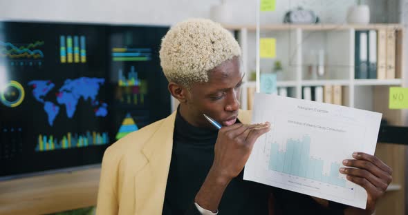 Man Talking and Showing Sheet of Paper with Graphs for Colleagues Looking at laptop alt