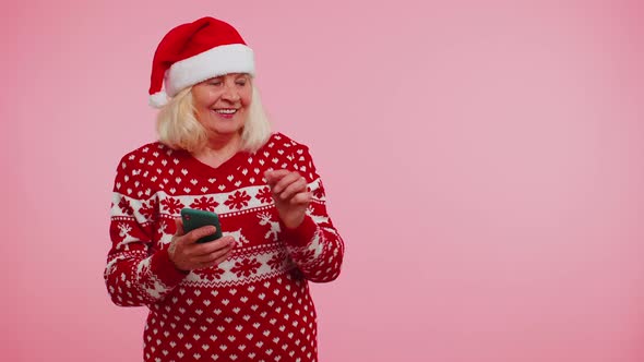 Grandmother Santa Christmas Sweater with Mobile Phone Showing Pointing Empty Place Advertising Area alt