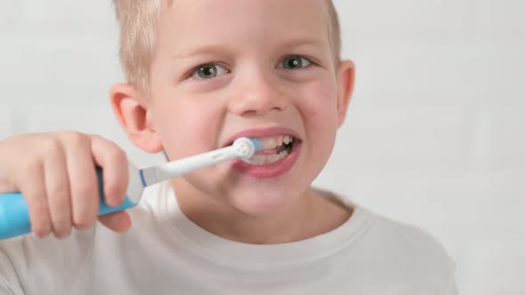 Portrait Happy Smiling Child Kid Boy Brushing Teeth with Electric Toothbrush on White Brick alt