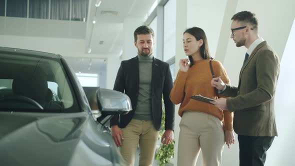 Young Family Purchasing Automobile in Car Dealership Talking To Sales Manager alt