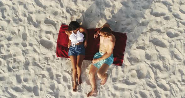Top view of couple lying on white sand beach taking a sunbath in summer
