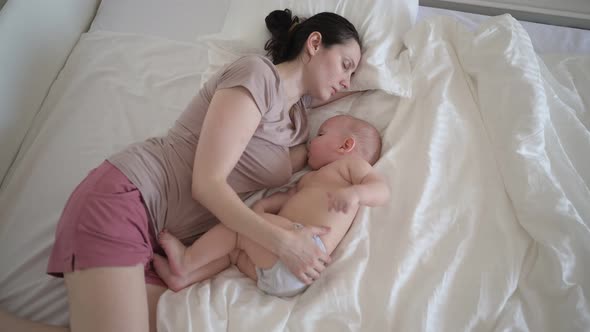 Tired Mother Sleeping with Newborn Cute Infant Naked Baby Boy on Bed Holding Him on Arms Hugging and