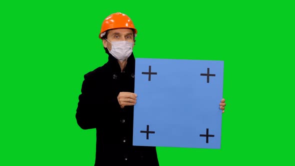 Portrait Of An Engineer In Hard Hat And Mask Holding Blank Board on Green Screen