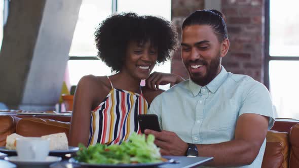 Diverse male and female colleagues sitting in cafe using a samrtphone having a discussion alt