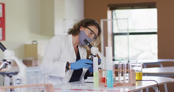 Female teacher wearing face mask using microscope at laboratory at school alt