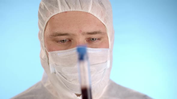Man in protective suit, medical mask, gloves shows test tube with Coronovirus