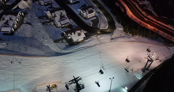 Aerial View of Skiers Go Down Ski Slopes Near Ski Lifts on Ski Resort at Night. alt