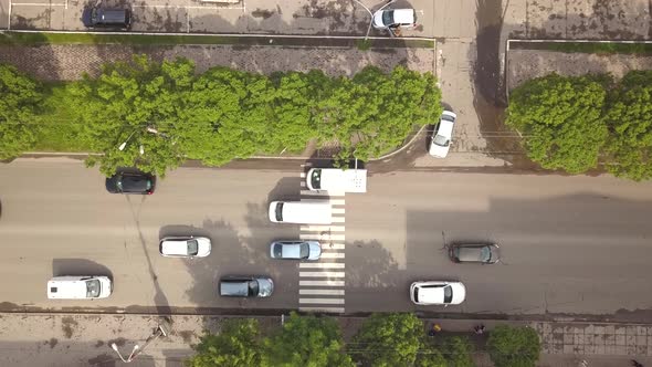 Top down aerial view of street with moving cars and zebra crosswalk with crossing pedestrians alt