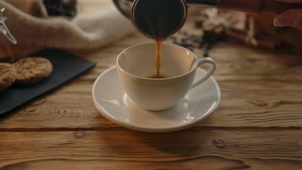 Pouring Coffee From the Cezve Into a Cup on a Wooden Table alt