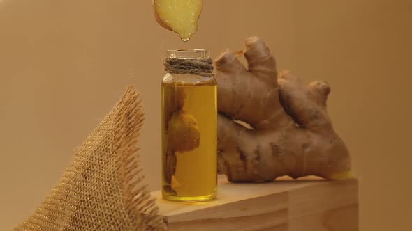 Glass Bottle of Essential Ginger Oil Dripping Ginger Root on Beige Background alt