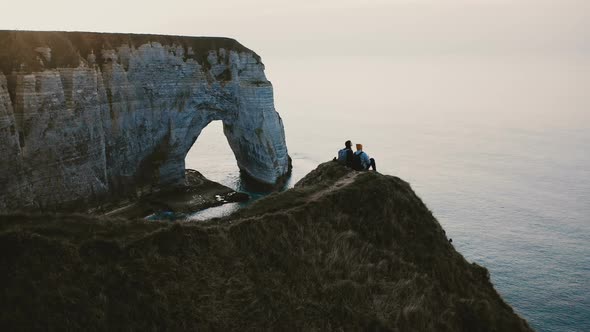 Beautiful Drone Panning View of Happy Friends Couple Sitting Together Watching Sunset Sea  alt
