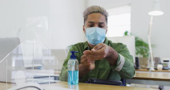 Man wearing face mask sanitizing his hands at office alt