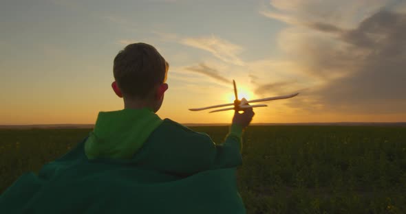 A Boy Is Running Across a Field with a Plane in His Hand. Sunset.  alt