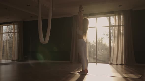A Young Woman in White Sportswear is Stretching with a Large Hall with Large Windows in a Slowmotion alt
