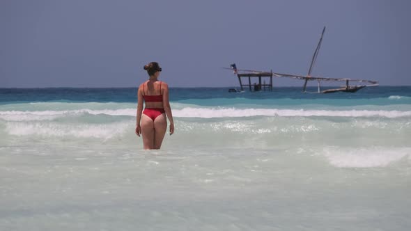 Young Woman in a Red Swimsuit Walks Into the Turquoise Ocean on a Paradise Beach alt