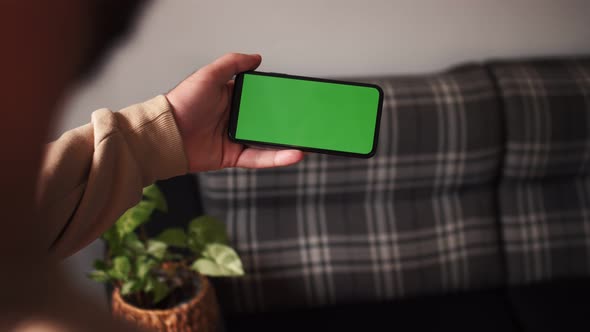 Handheld Camera: Point of View of Man at Modern Room Sitting on a Chair Using Phone With Green Mock alt