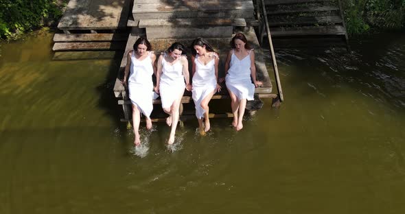 Girls In White Dresses Sit On The Pier And Splash In The Water alt